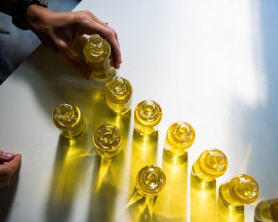 a hand touching glass bottles filled with herbal-infused golden body oil on a white table. 