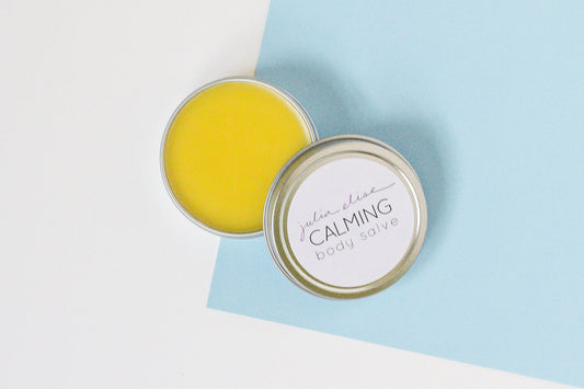 open tin of calming body salve showing golden yellow herbal-infused salve in the tin. the tin is on a light blue and white background